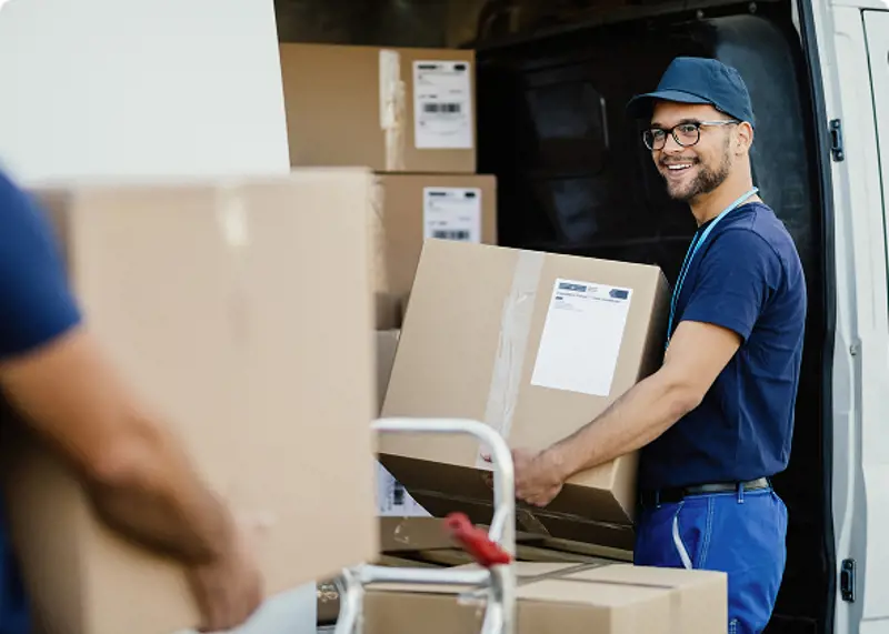 young-happy-manual-worker-carrying-cardboard-boxes-delivery-van-while-communicating-with-his-colleagues-1